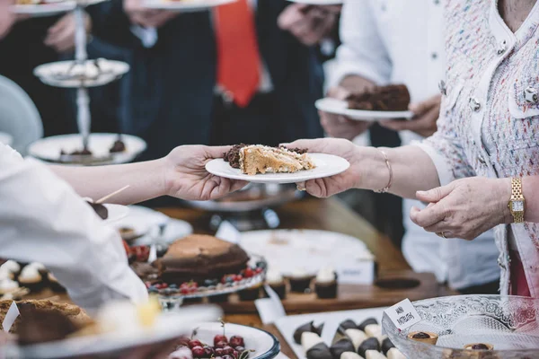 Display of sweet desserts at a celebration. People are served desserts on the plates.