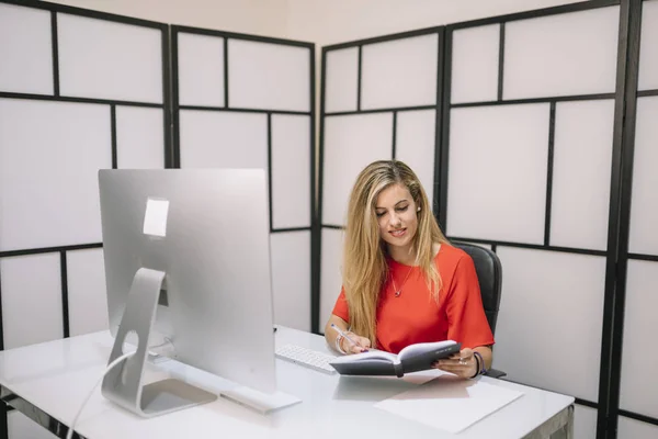 Pretty blonde woman works in office with computer.
