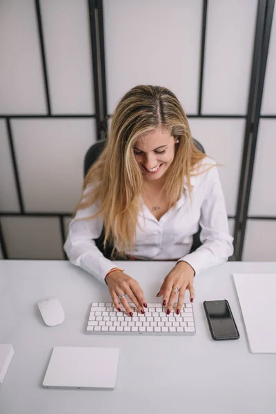 Pretty blonde woman works in office with computer.