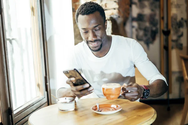 African man consults the cell phone while having a coffee.
