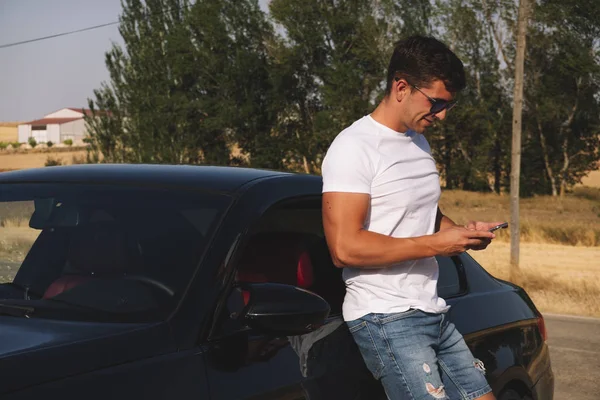 Young man phone poses with his car