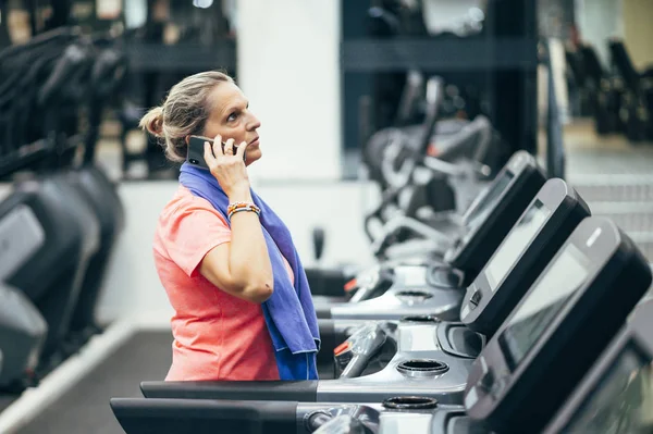 Retired senior woman using phone in gym