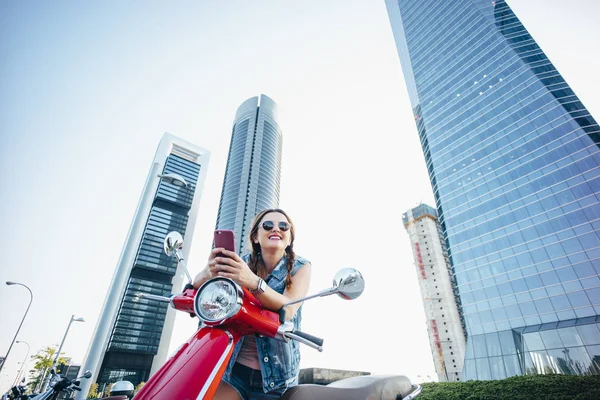 Pretty young woman on motorcycle in front of tall skyscraper bui