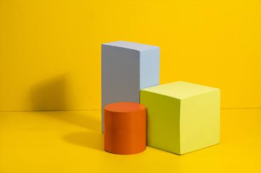 Sarı arka planda farklı renklerde geometrik şekiller. Renkli kağıt üzerinde üç boyutlu katı rakamlar.