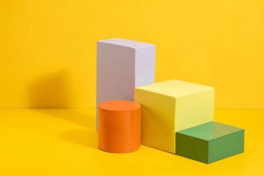 Sarı arka planda farklı renklerde geometrik şekiller. Renkli kağıt üzerinde üç boyutlu katı rakamlar.