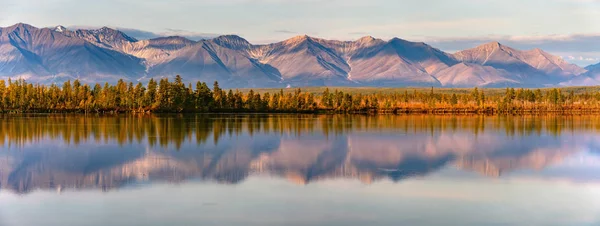 Reflection of mountains on a calm lake at sunset or sunrise. Panorama of autumn landscape in Yakutia, Sakha Republic, Russia. Beautiful scenery sunrise view of lake and reflection in water