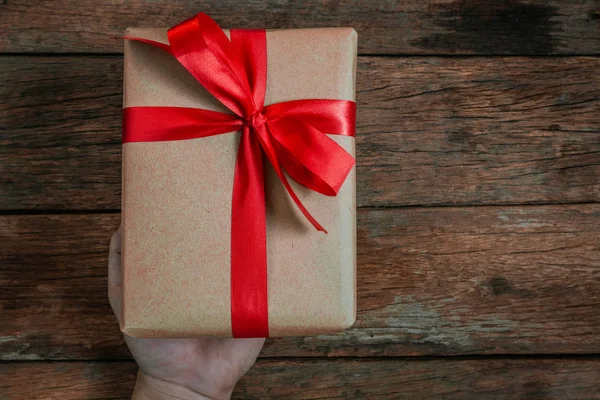 奖金人类的手给礼物棕色礼物盒领结红色丝带在老木地板上的顶部看法快乐圣诞节和快乐的新年概念 — 图库照片
