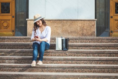 şapka ve güneş gözlüğü güzel esmer kız telefonu el ve gülümsüyor adımlarla oturur.