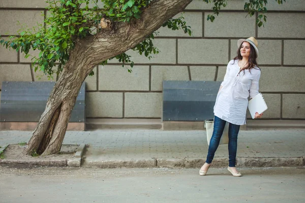 Bir deposundan laptop ve paketleri ile sokakta yürürken şapkalı gülümseyen güzel esmer kız