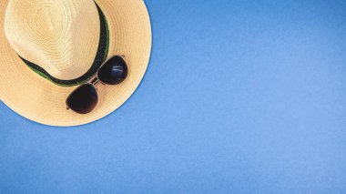 hasır şapka mavi bir arka plan üzerinde güneş gözlüklü. Üstten görünüm boşaltmak afiş kavramı