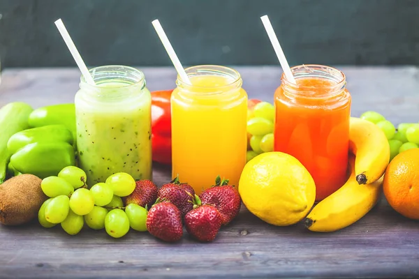 freshly squeezed fruit juice, smoothies yellow orange green blue banana lemon apple orange kiwi grape strawberry on a dark wooden background Copy space