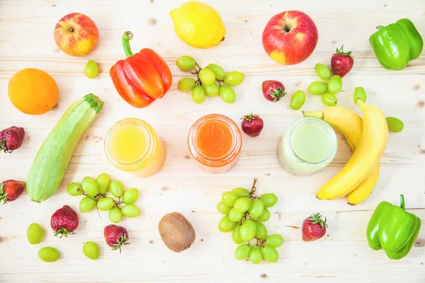 freshly squeezed fruit juice, smoothies yellow orange green blue banana lemon apple orange kiwi grape strawberry on a light wooden background Close up Flat lay.