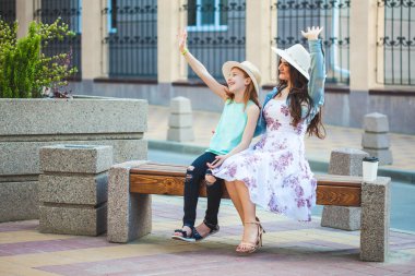 iki kız kardeş, bir güzel esmer kız ve Genç kız yürüyerek şehir, bir bankta oturup ve konuşmak, gülmek ve ellerini dalga