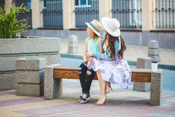 Dos hermanas, una hermosa morena y una jovencita caminando por la ciudad, sentadas en un banco y hablando, riendo — Foto de Stock