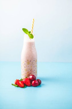 Güler yüzlü şişeyle yapılan süt, kiraz, çilek, muz ve parlak mavi arka plan sağlıklı yaşam konsepti üzerine nane ile dekore edilmiştir. Vücut kopya alanı temizliği