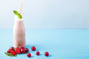Güler yüzlü şişeyle yapılan süt, kiraz, çilek, muz ve parlak mavi arka plan sağlıklı yaşam konsepti üzerine nane ile dekore edilmiştir. Vücut kopya alanı temizliği.