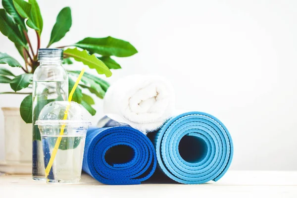 set for sports, blue yoga mat towel and a bottle of water on a light background The concept of a healthy lifestyle. Copy space