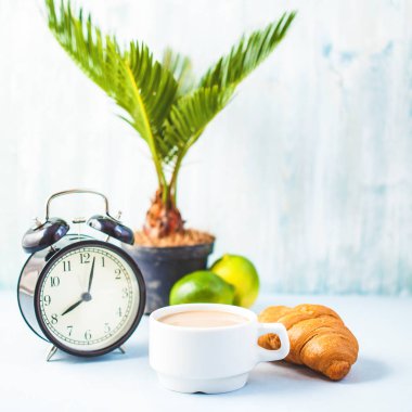 sabah kahve ile bir çalar saat kahvaltı neşe, sağlıklı kahvaltı tazelik kopya spase hafif bir arka plan uyandırma üzerinde beyaz bir fincan kruvasan.