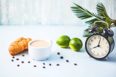 sabah kahve ile bir çalar saat kahvaltı neşe, sağlıklı kahvaltı tazelik kopya spase hafif bir arka plan uyandırma üzerinde beyaz bir fincan kruvasan kireç.