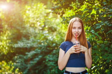 Genç güzel kız sulu yeşillik bir arka plan üzerinde taze sıkılmış meyve suyu içecekler.