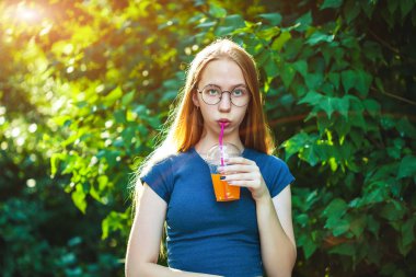 Genç güzel kız sulu yeşillik bir arka plan üzerinde taze sıkılmış meyve suyu içecekler.