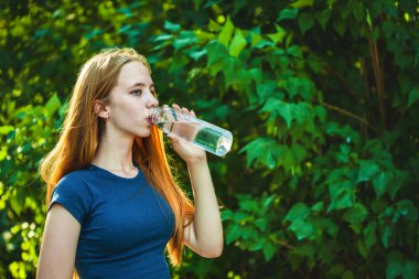 sportif genç kız parlak yeşillik bir arka plan üzerine bir şişe suyu içer.