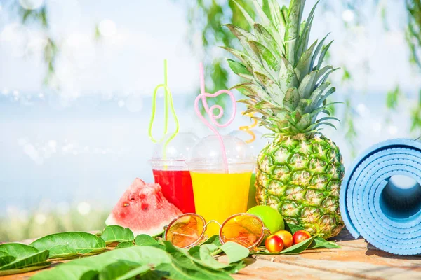 Parlak taze sağlıklı meyve suları, meyve, ananas, karpuz. deniz arka plan üzerinde güneş gözlüğü yoga mat. Summer, dinlenme, sağlıklı yaşam tarzı kopya alanı