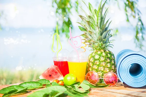 Parlak taze sağlıklı meyve suları, meyve, ananas, karpuz. deniz arka plan üzerinde güneş gözlüğü yoga mat. Summer, dinlenme, sağlıklı yaşam tarzı kopya alanı