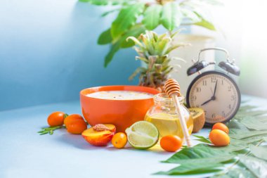 Yararlı sabah kahvaltı, müsli, meyve şeftali kireç ananas bal fincan kahve ve bir çalar saat üzerinde mavi bir arka plan kopya alanı
