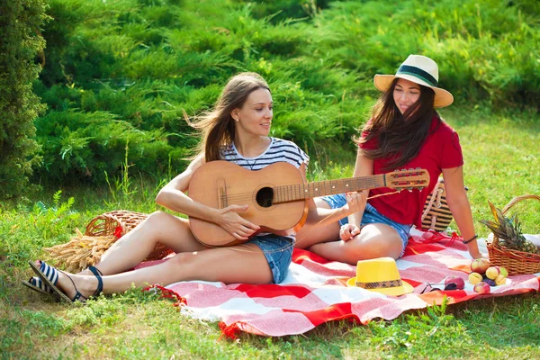 Two beautiful young women on a picnic playing a guitar and having fun Close up