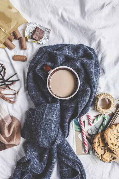 Winter cozy concept. Cup with coffee , cookies, gift , fir branch, plaid on the bed Christmas card mockup