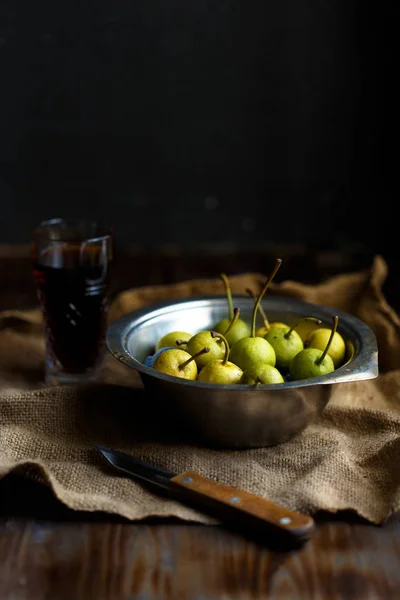 Wild pear in a metal bowl and a glass of homemade pear wine on a wooden close background. Rustic concept. The harvest is delicious
