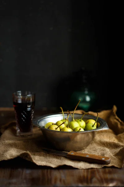 Wild pear in a metal bowl and a glass of homemade pear wine on a wooden close background. The harvest is delicious Rustic style