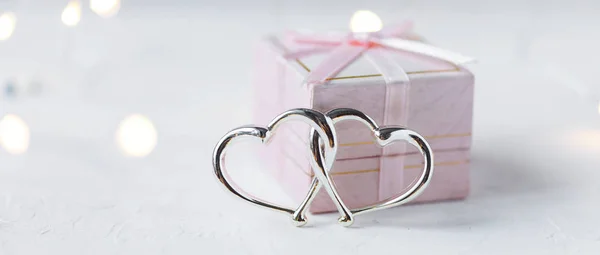 Gift box, decorative hearts and lights on a light background. Valentine\'s day concept Copy space Banner Selective focus