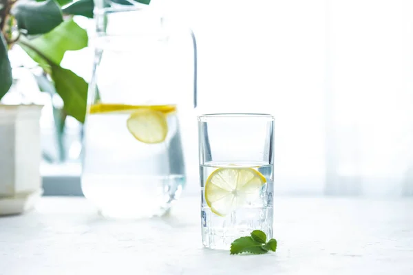 glass cup and a carafe of water, ice, mint and lemon on a white table Copy space