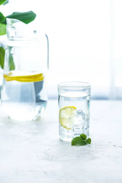 glass cup and a carafe of water, ice, mint and lemon on a white table Copy space