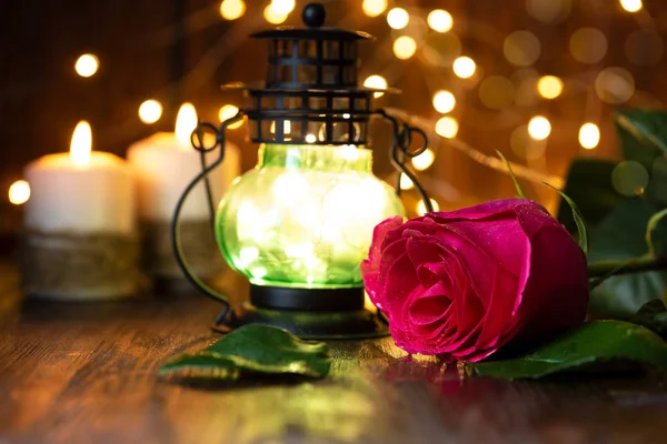 red rose and lantern with lights on a wooden table.