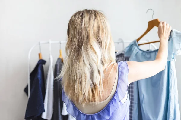 Blondy girl near a wardrobe with clothes can not choose what to wear