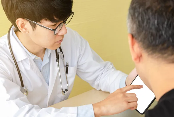 Junge asiatische Arzt erklärt mit männlichen Patienten über digitale ta Stockbild