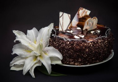 siyah bir arka plan üzerine krema çikolata küçük pasta beyaz zambak ile süslenmiş