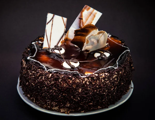 small chocolate cake with frosting and decorations of white chocolate on a black background