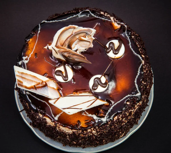 small chocolate cake with frosting and decorations of white chocolate on a black background