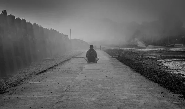 Dramatic fog scene with a man sitting alone.