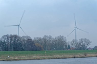 İki rüzgar türbinleri ağaçların üzerinden sisli gün döndürün. Hamburg, Almanya