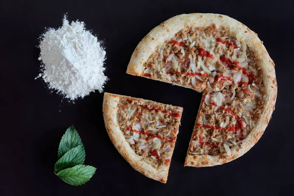 Fırında ton balığı pizza, un ve siyah arka plan üzerine yeşil yaprak yığını