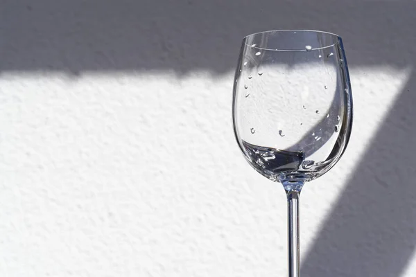 Copo de vinho vazio contra a parede branca no dia ensolarado — Fotografia de Stock