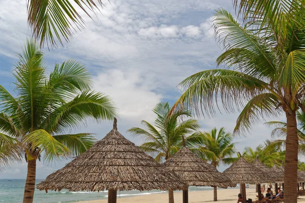 Sombrillas de paja en medio de palmeras en la playa de arena — Foto de Stock