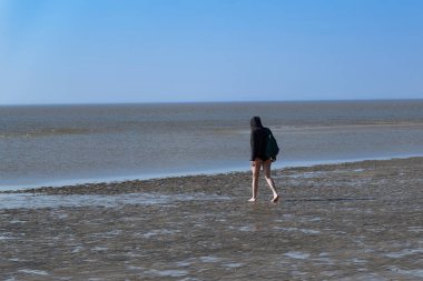 Paltolu ve çıplak bacaklı bir kadın kumsalda yürüyor.