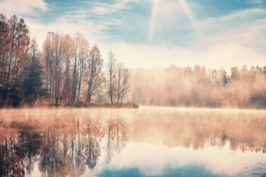 Sonbahar sabahı manzarası. Orman göl, yoğun sis, yükselen güneşin kirişler yansıtılır.