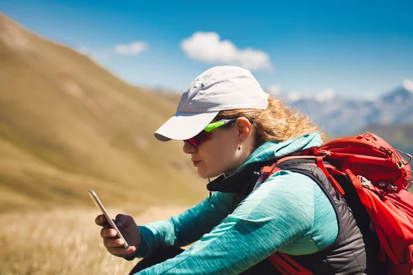 Junges Mädchen mit Rucksack in den Bergen unterwegs mit Smartphone. — Stockfoto